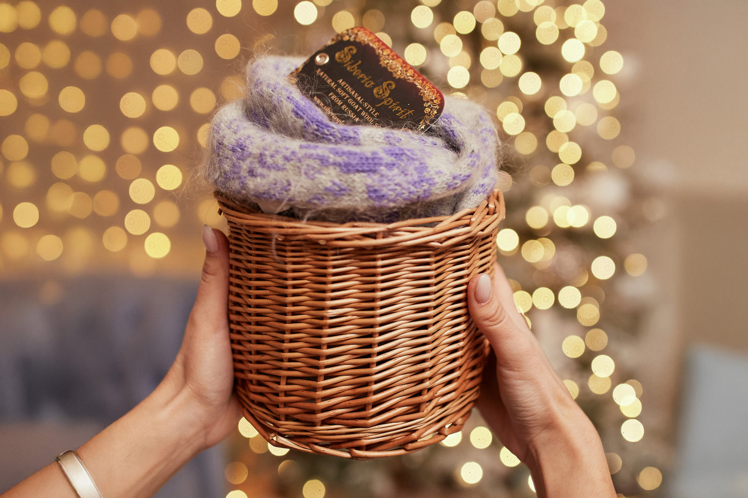 Wicker basket with a purple item and a tag, held against a blurred festive background.