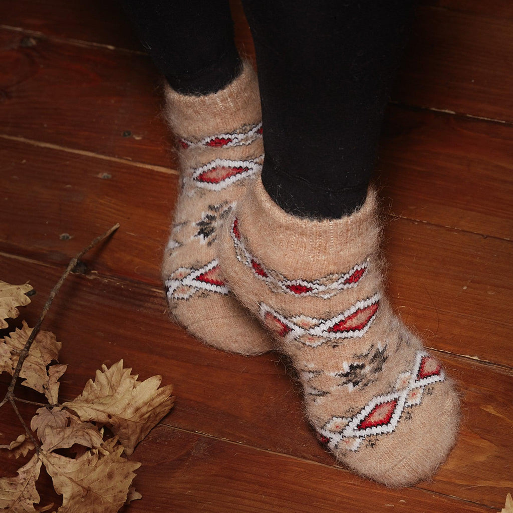Woman's feet wearing black leggings and warm-beige low-cut thick wool socks with red, black, and white geometric designs.