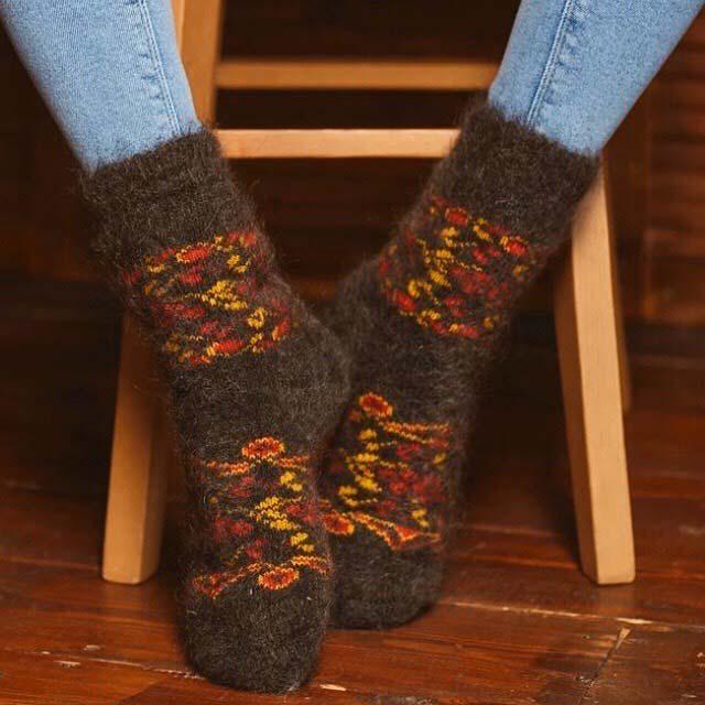 Woman’s legs sitting on a chair wearing jeans and goat hair black crew home socks with red berries and yellow leaves.
