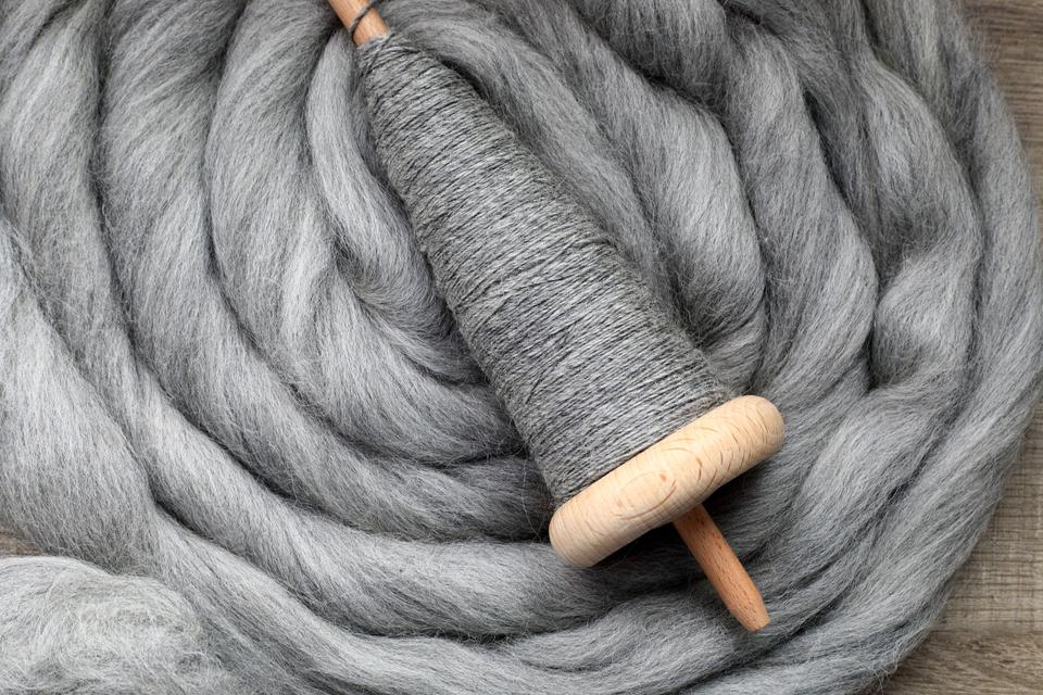 Wooden spindle with grey yarn laying on top of grey yarn.