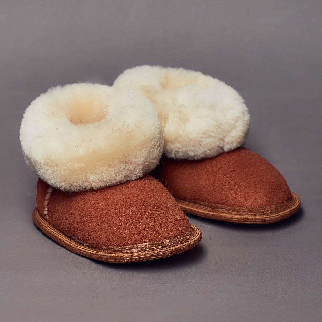 Camel color sheepskin slippers for toddlers on grey background.