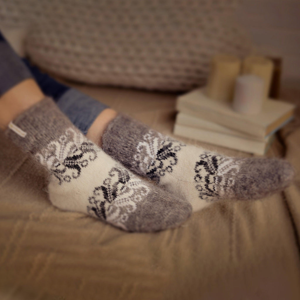 Woman's feet on a bed wearing white and gray goat hair crew socks.