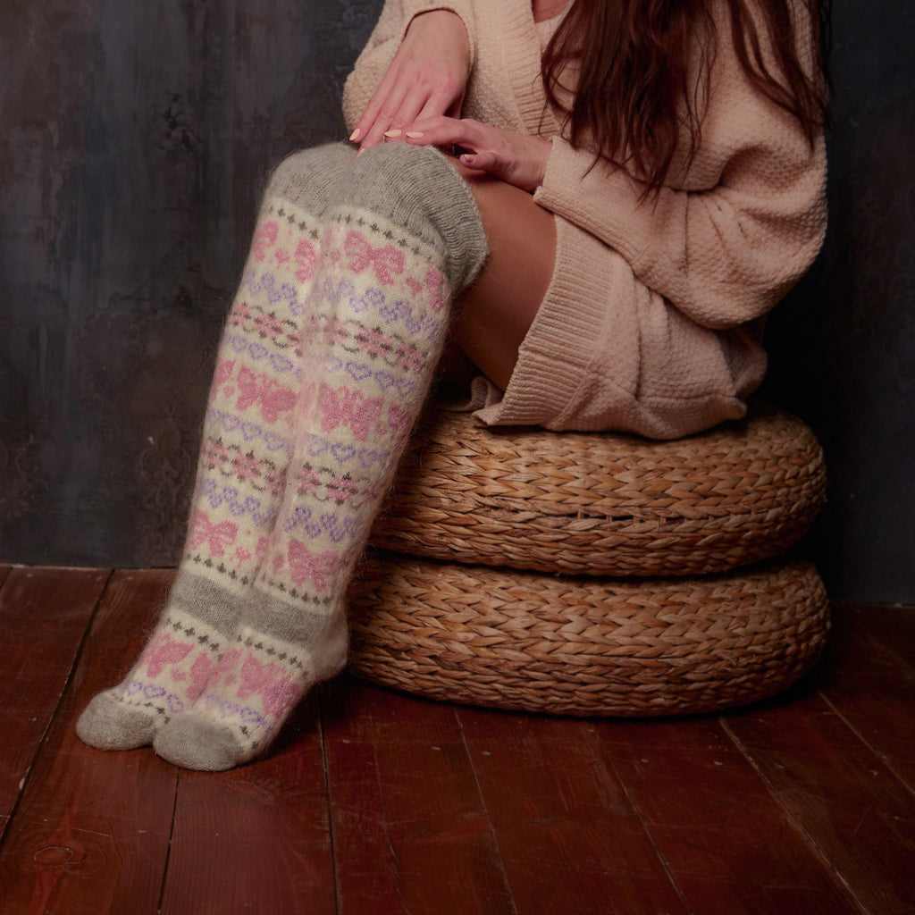 Woman sitting on a wicker chair wearing over-the-knee goat hair grey, white, and pink socks.