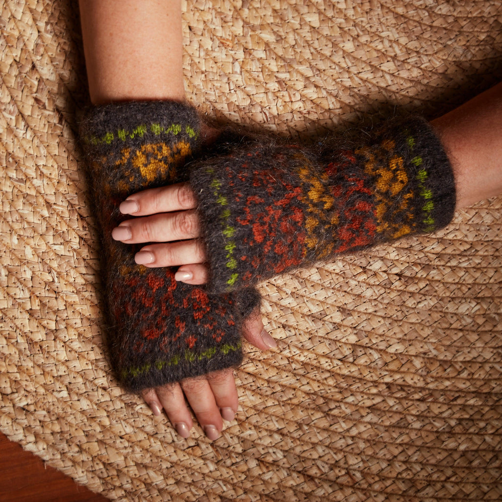 Woman's hands wearing black fingerless gloves with green, orange, and yellow fall leaves design.
