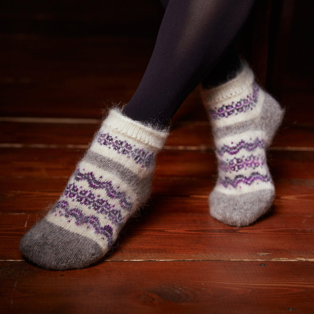 Woman's legs wearing black pantyhose and white grey low-cut goat hair socks with purple ornament. 