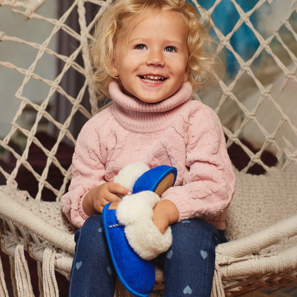 Child sitting on chair holding blue sheepskin toddler's slippers.
