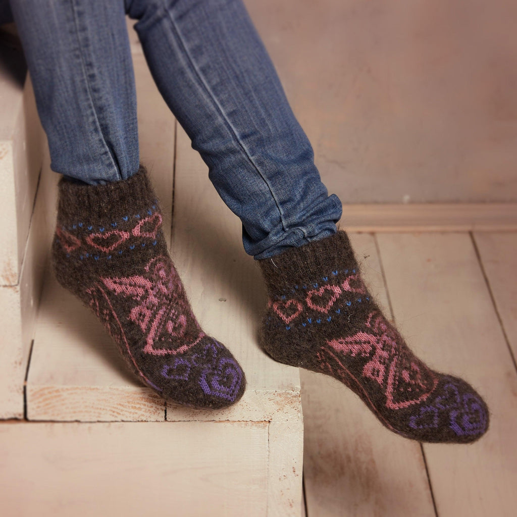 Woman’s legs wearing jeans and low-cut warm goat hair black, pink, and purple socks with angels and hearts pattern.