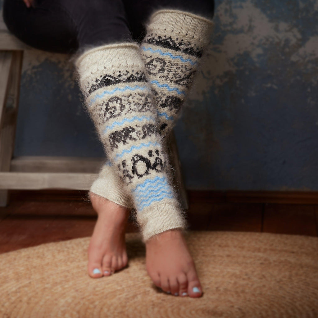 Woman's legs wearing black pants and warm, fuzzy goat hair white and blue leg warmers with black mountains, owls, bears, and penguins.