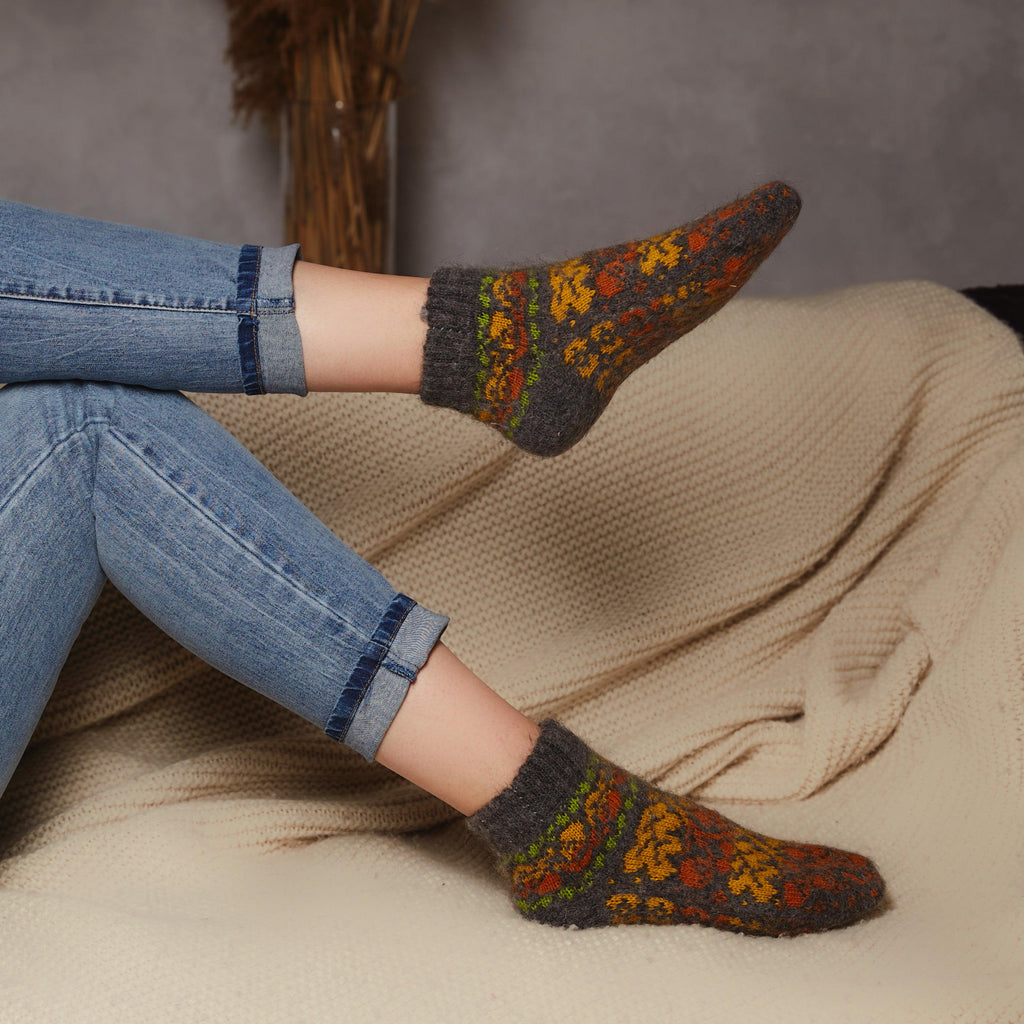 Woman's legs on the couch wearing jeans and dark low-cut goat wool warm socks with autumn leaves design.