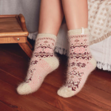 Woman’s legs standing by the bed wearing white and pink goat hair thick crew socks.