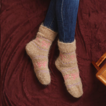 Woman's legs on the bed wearing jeans and beige crew goat wool socks with pastel butterflies and hearts design.