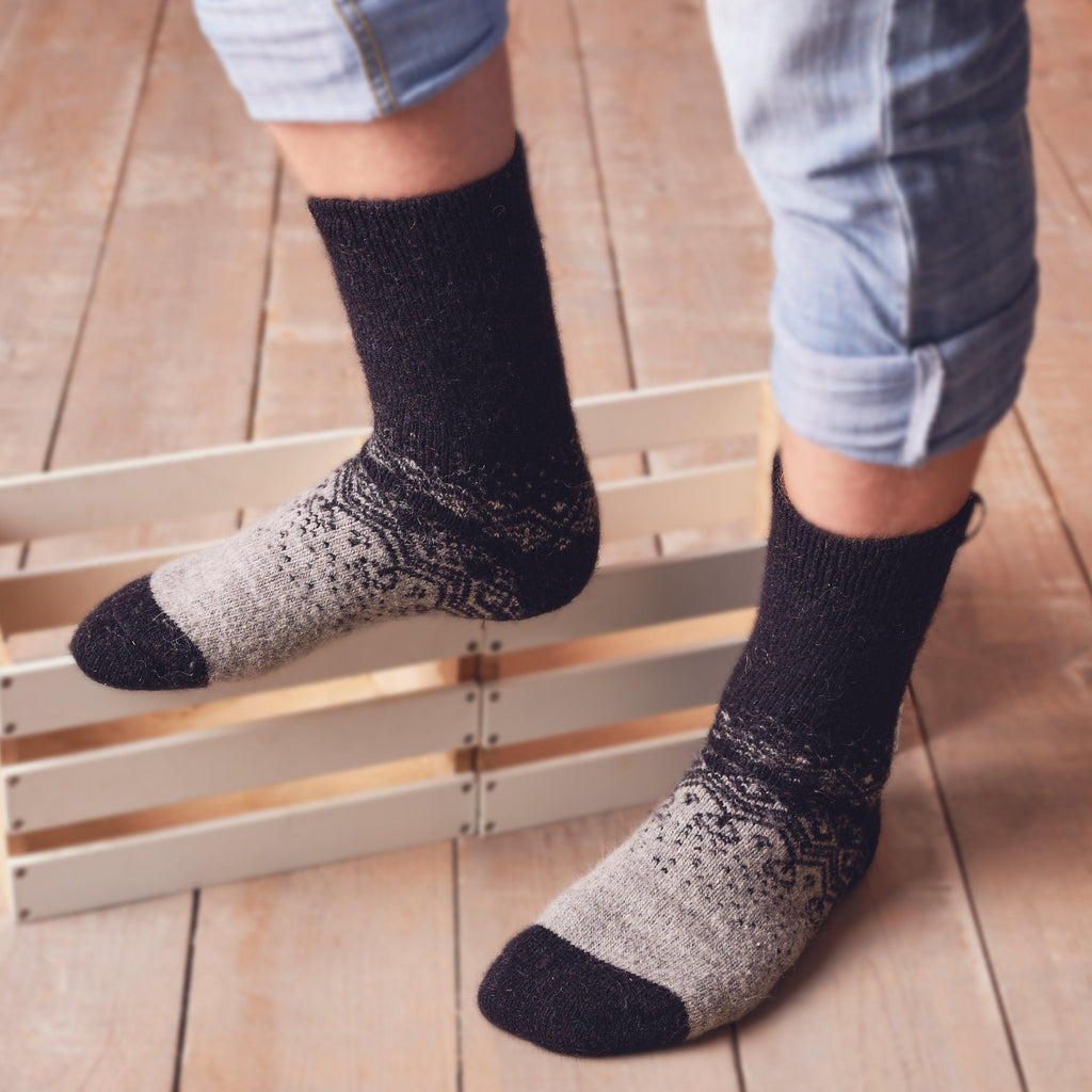 Man’s legs in home interior wearing warm merino wool grey-black socks with ornament.