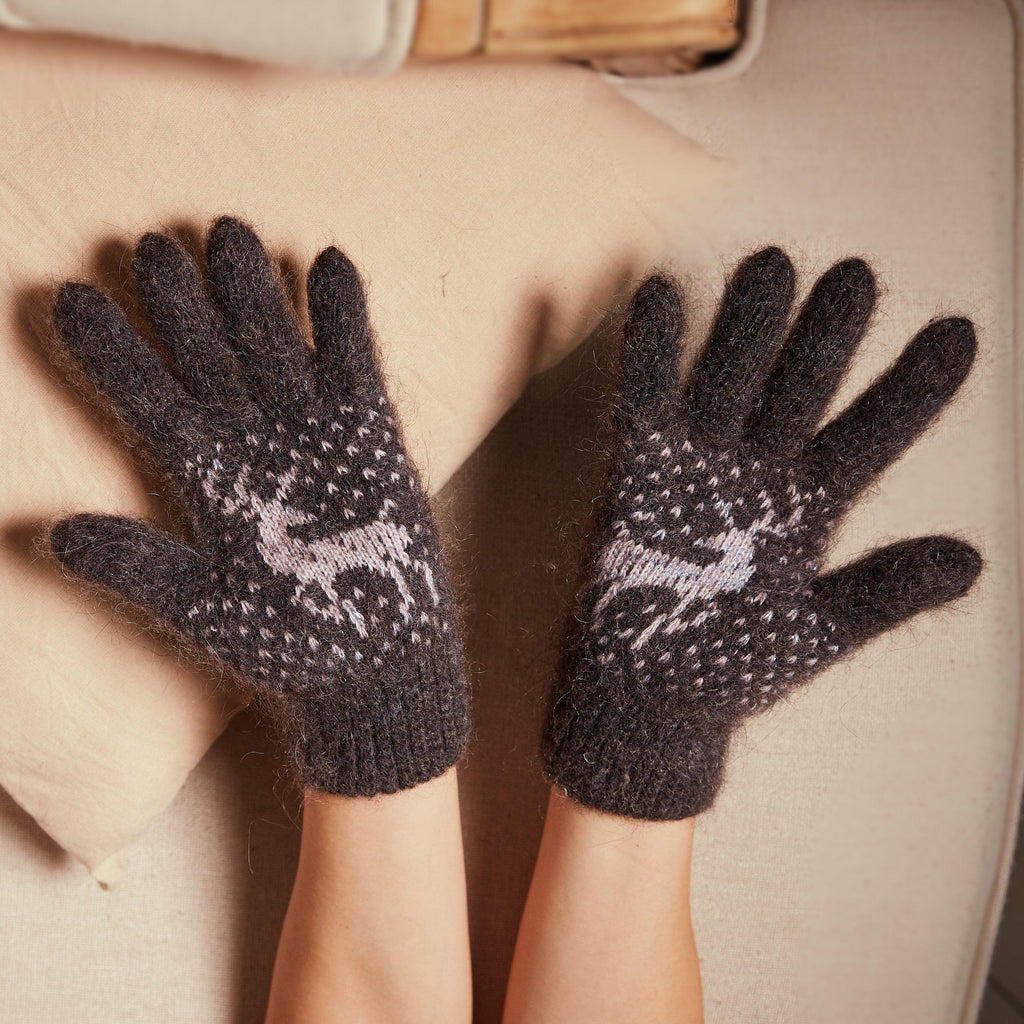 Person's hands wearings charcoal thick goat hair winter gloves with a light-gray stag design.