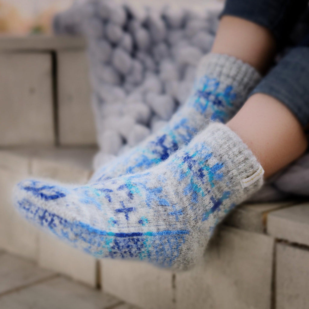Person's feet wearing gray goat hair low-cut socks with multicolor blue snowflake design.