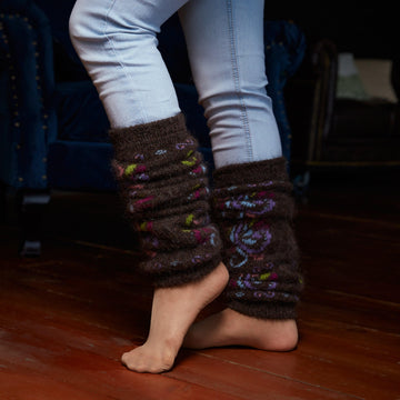 Woman’s legs wearing jeans and goat hair thick black leg warmers with blue, green, and purple swirls.