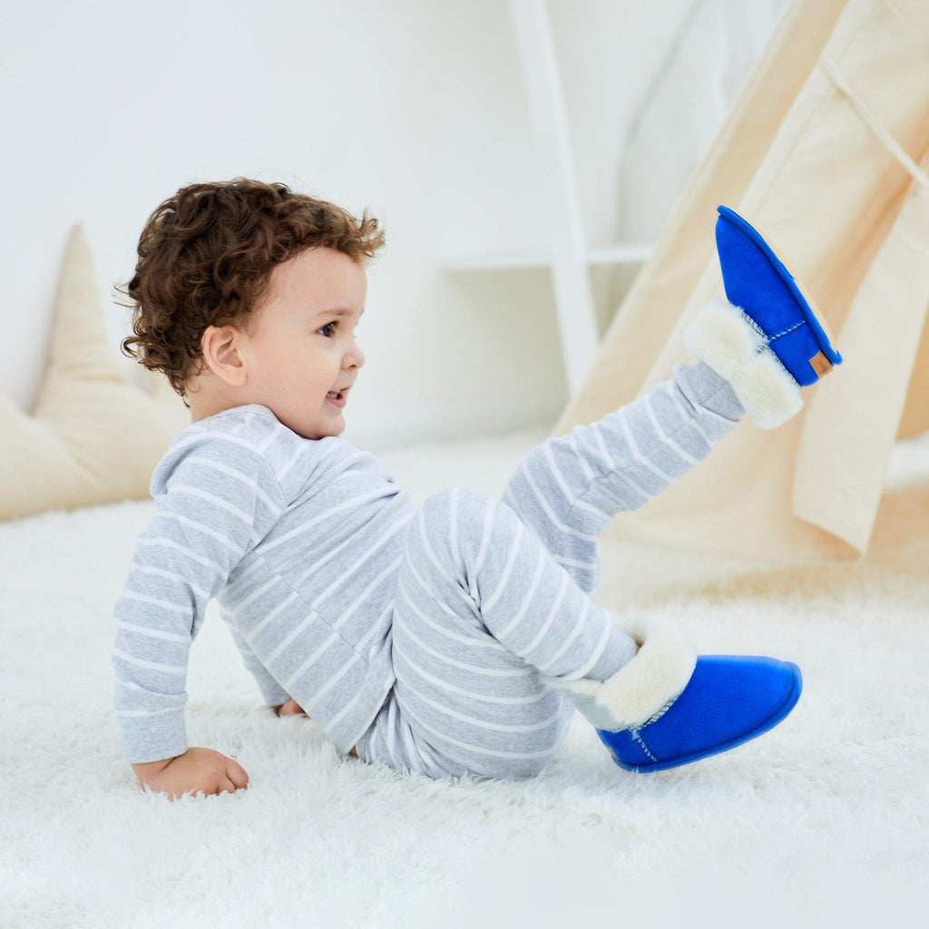 Boy wearing blue sheepskin toddler slippers with white fur.