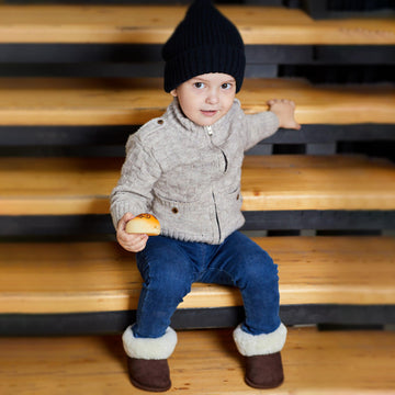 Boy sitting on the stairs wearing brown sheepskin toddler slippers with white fur.