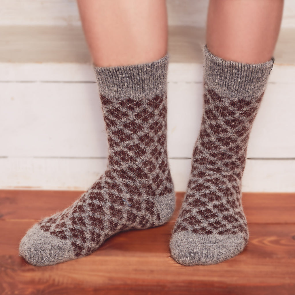 Man’s legs standing wearing grey thick wool socks with a brown diamond-shaped pattern.