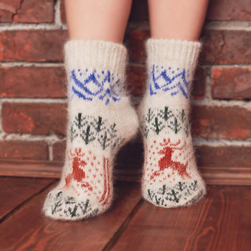 Woman’s legs wearing low-cut warm off-white goat wool socks with a brown deer, green forest, blue mountains design.