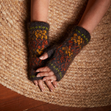 Woman wearing fuzzy warm goat wool black fingerless gloves with yellow and orange fall leaf pattern.