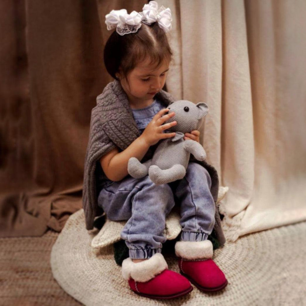 Girl wearing pink sheepskin toddler slippers with white fur.