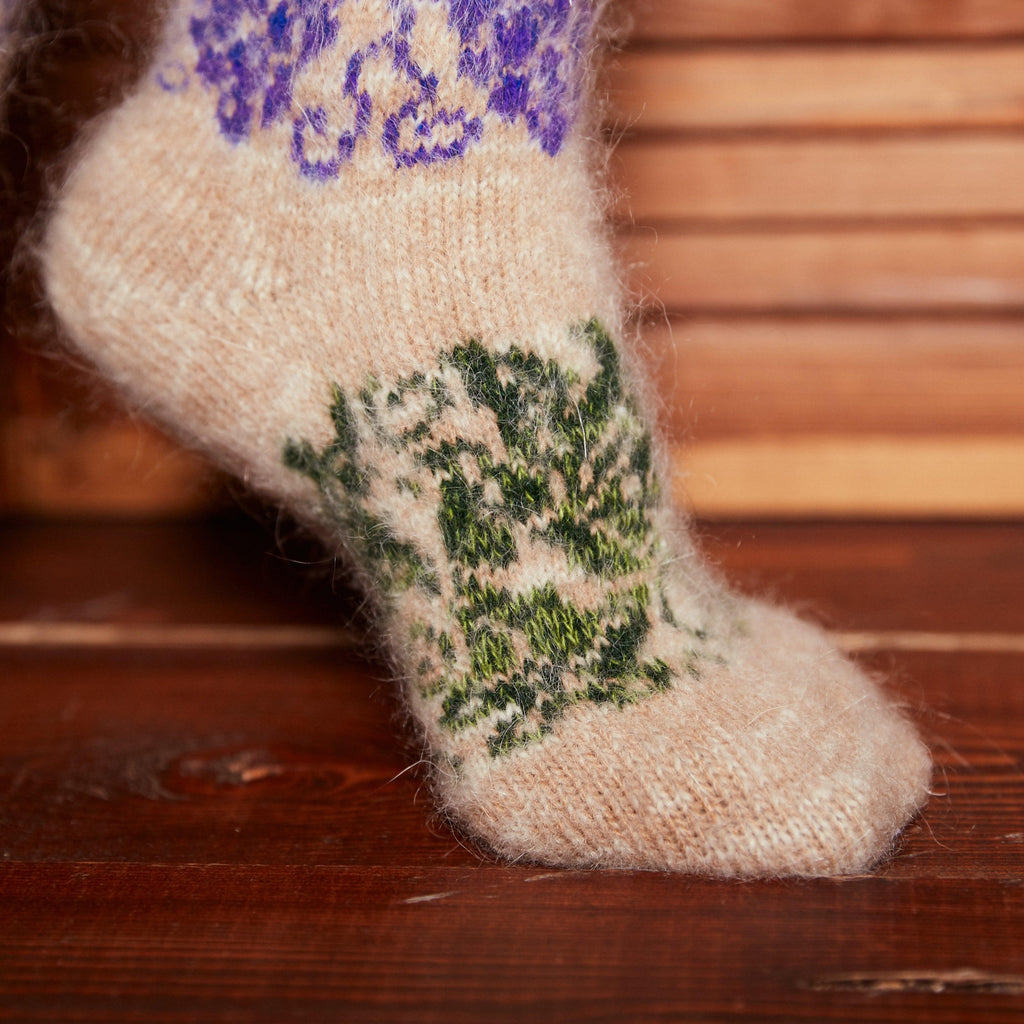 Foot wearing a beige goat hair sock with grapes and leaves purple-green design.