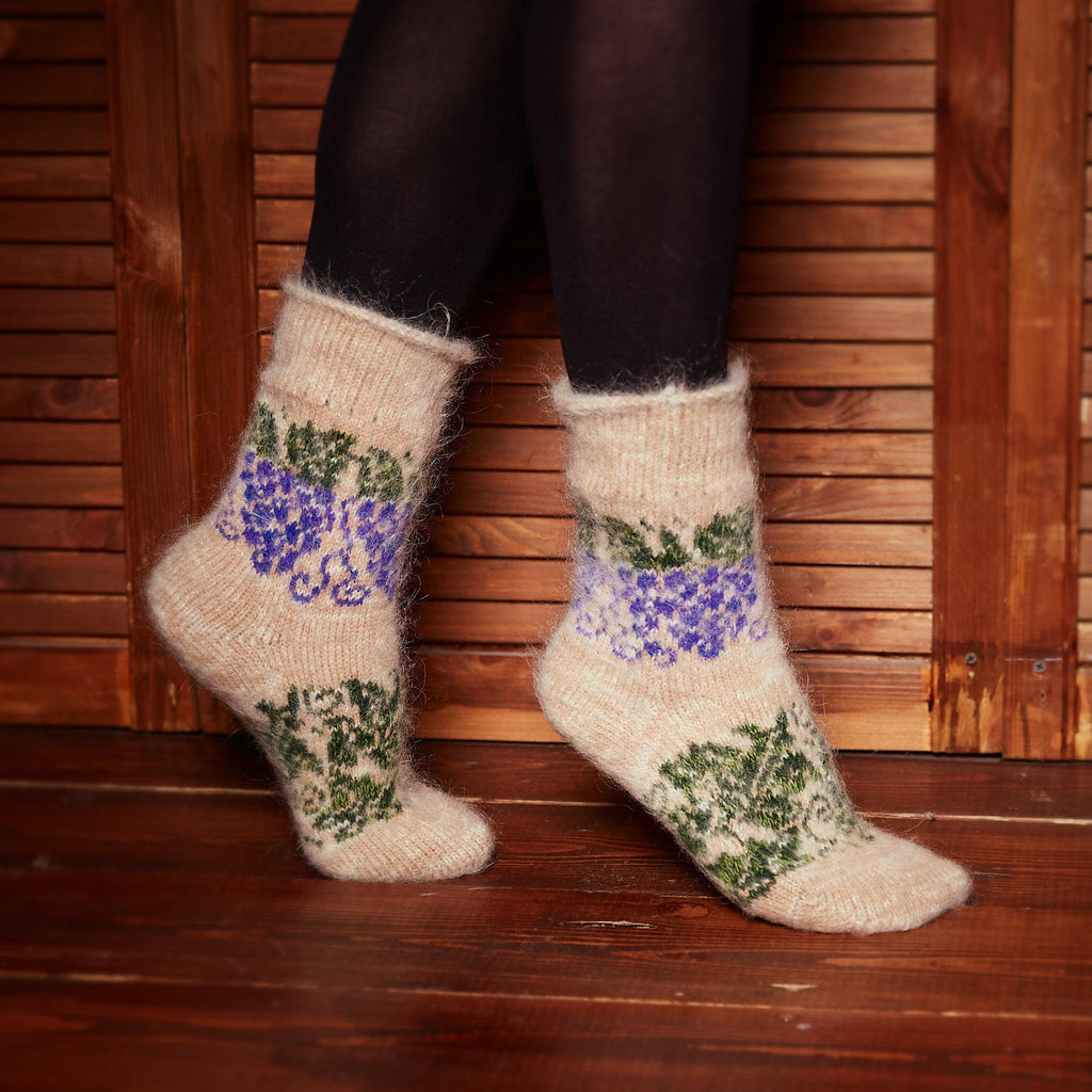 Woman’s legs standing on the wooden floor wearing leggings and beige crew wool socks with a green and purple grape design.