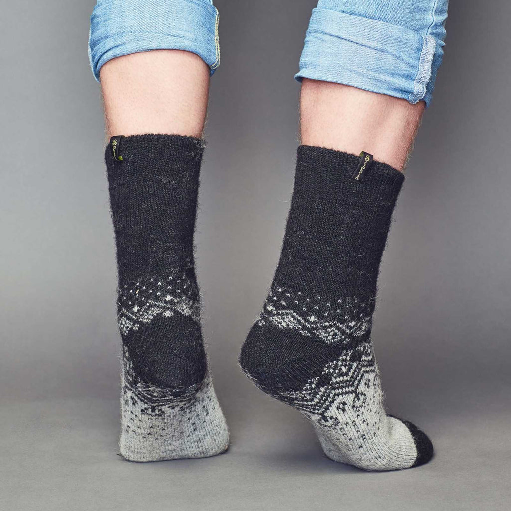 Man’s legs wearing blue jeans and warm merino grey and black socks with ornament - back view.