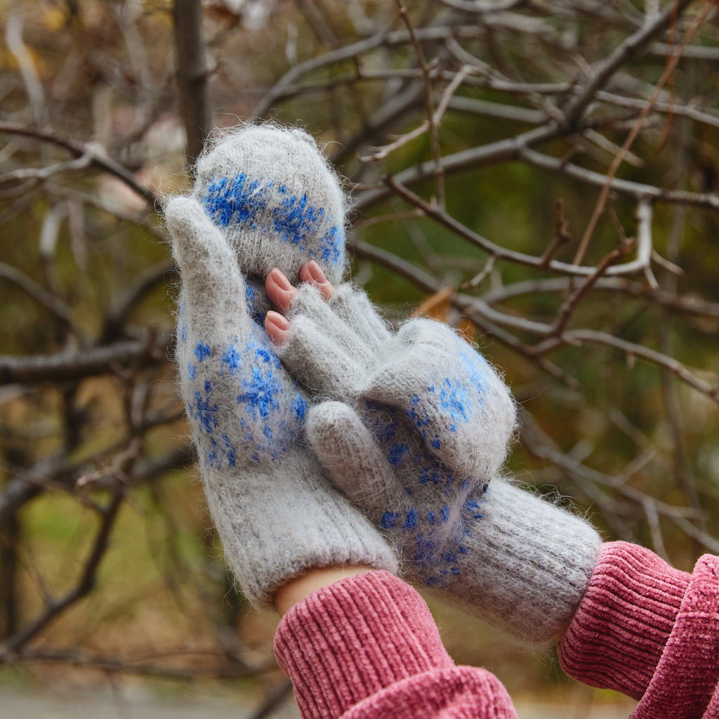 Person wearing gray fingerless goat hair gloves with a flip with blue snowflakes design.