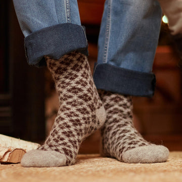 Man's legs wearing blue jeans and gray merino wool crew socks with a brown pattern.