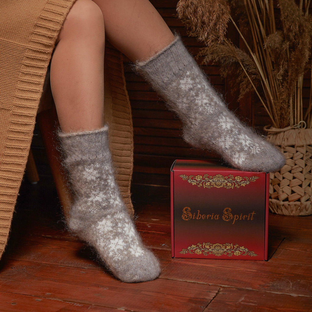 Woman's legs in home interior wearing gray relaxed-fit goat hair socks crew length with snowflake designs.