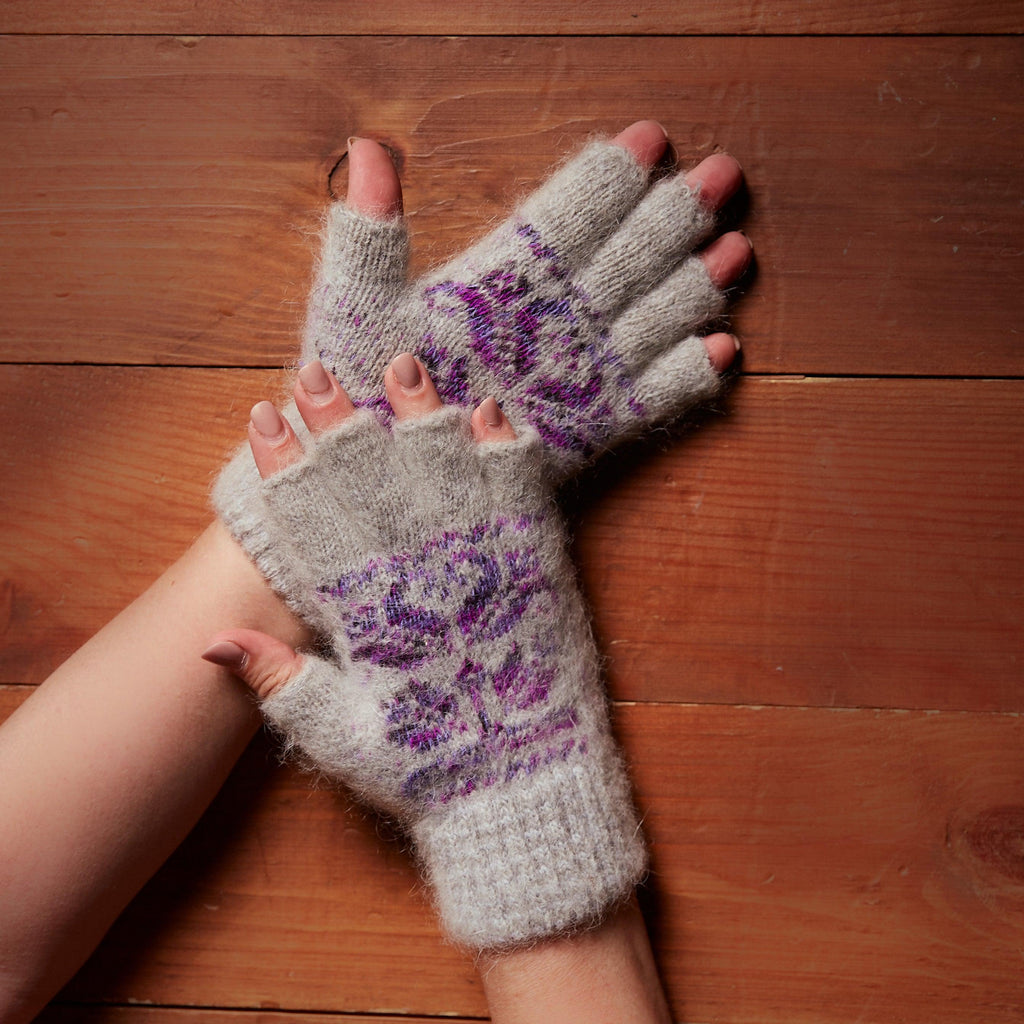 Person's hands wearing light-gray goat hair fingerless gloves with purple flower design.