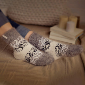 Woman's legs in home interior wearing jeans and white-and-gray relaxed fit goat hair socks with black ornaments.