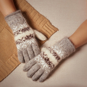 Woman’s hands wearing white and light-gray goat hair gloves with black and white snowflake design.