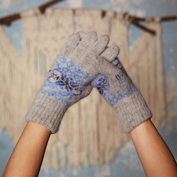 Woman's hands wearing gray goat hair winter gloves with a multi-blue snowflake design.