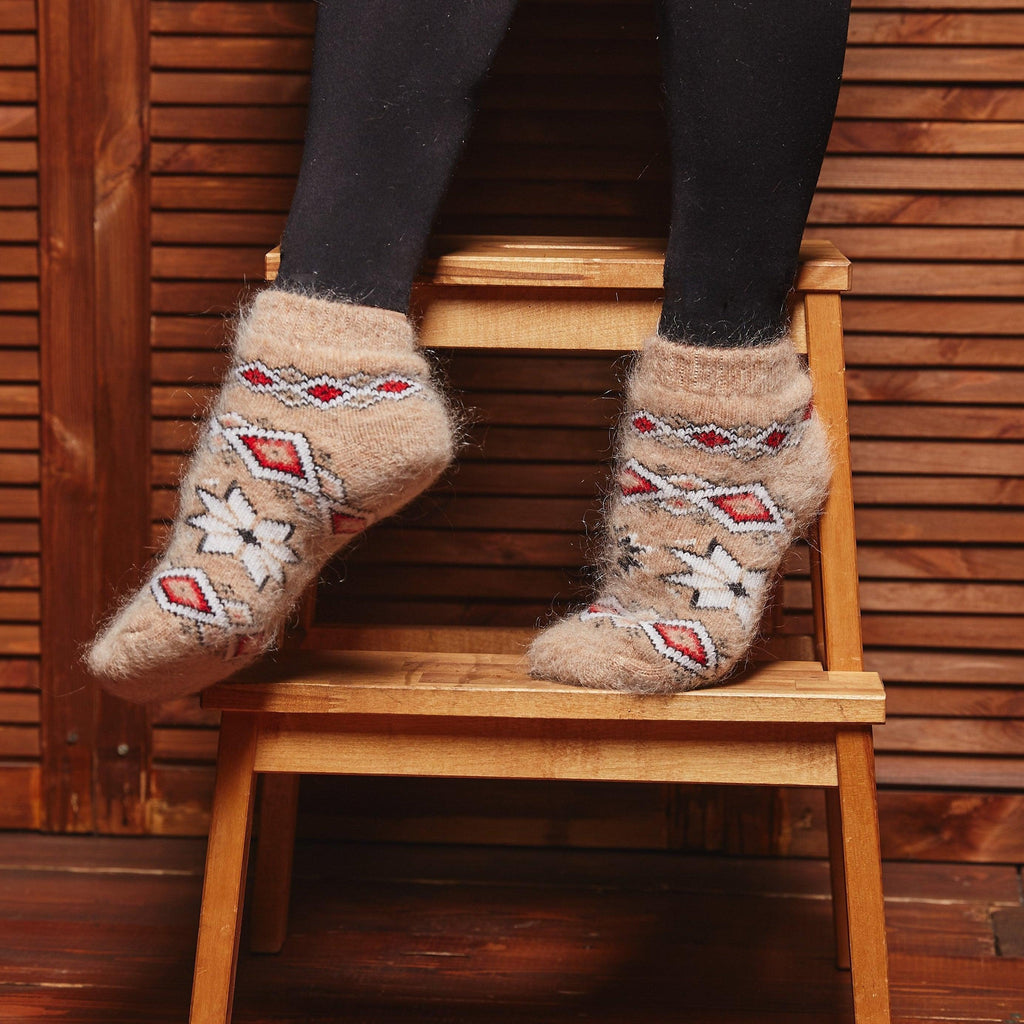 Woman’s legs standing on a chair wearing black leggings and warm goat hair light-brown socks with a western design.
