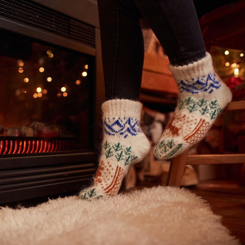 Woman’s legs wearing black leggings and low-cut warm goat wool socks with a brown deer, blue mountains, and green forest.