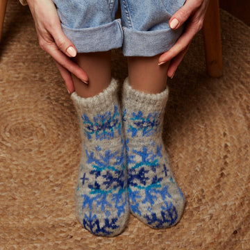 Woman’s legs wearing jeans and warm goat hair grey socks low-cut length with a large blue snowflake design.