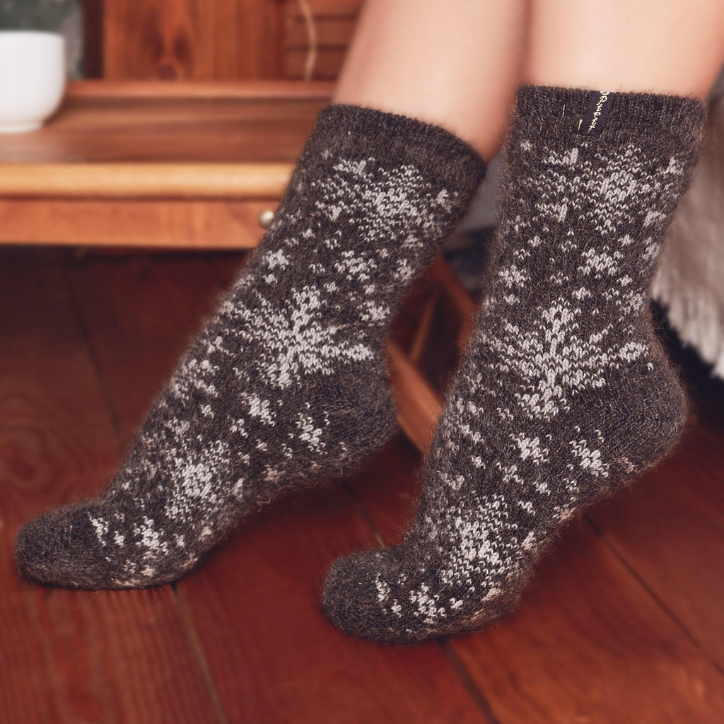 Woman’s legs posing by the bed wearing black wool warm socks crew length with white snowflake design.