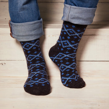 Man's legs wearing jeans and black merino wool crew socks with a blue diamond-shaped pattern.