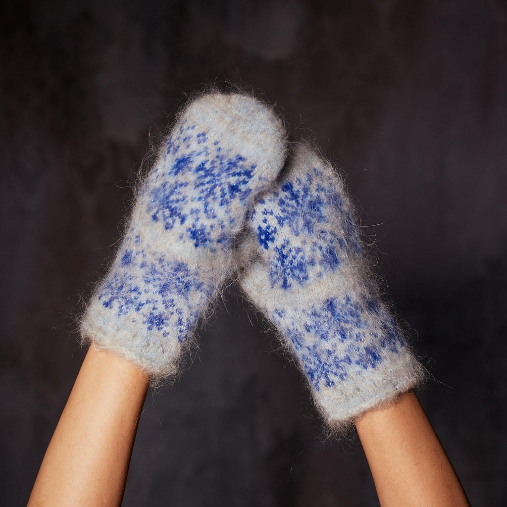 Person's hands wearing light blue goat hair mittens with blue snowflake design.