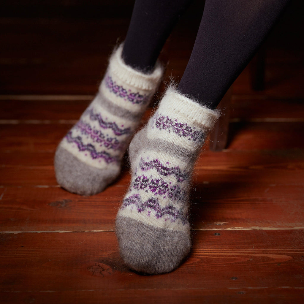 Woman's feet wearing gray and white no elastic low-cut goat hair socks with a multicolor purple design.
