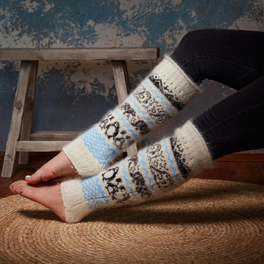 Woman's legs wearing black pants and white goat hair leg warmers with a black and blue arctic animals design.