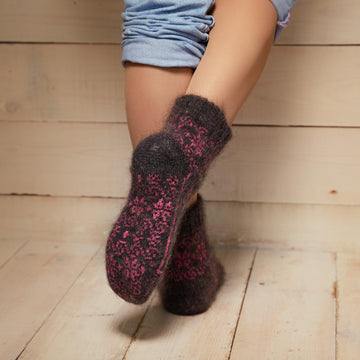 Woman's legs in home interior wearing black goat wool low-cut socks with pink designs - back view.