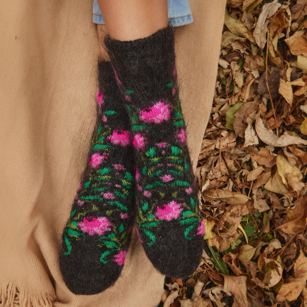 Woman's feet wearing black thick goat hair socks with pink peonies and green leaves design.