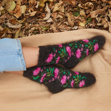 Woman's feet in outdoor settings wearing goat wool black crew socks with bright pink flowers.
