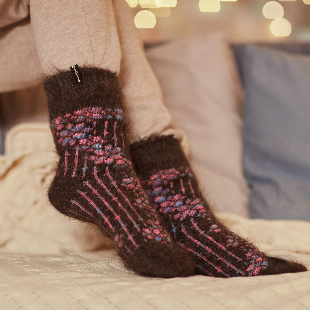 Woman's legs in home interior wearing grey pants and black goat hair crew socks with multicolor flower design.