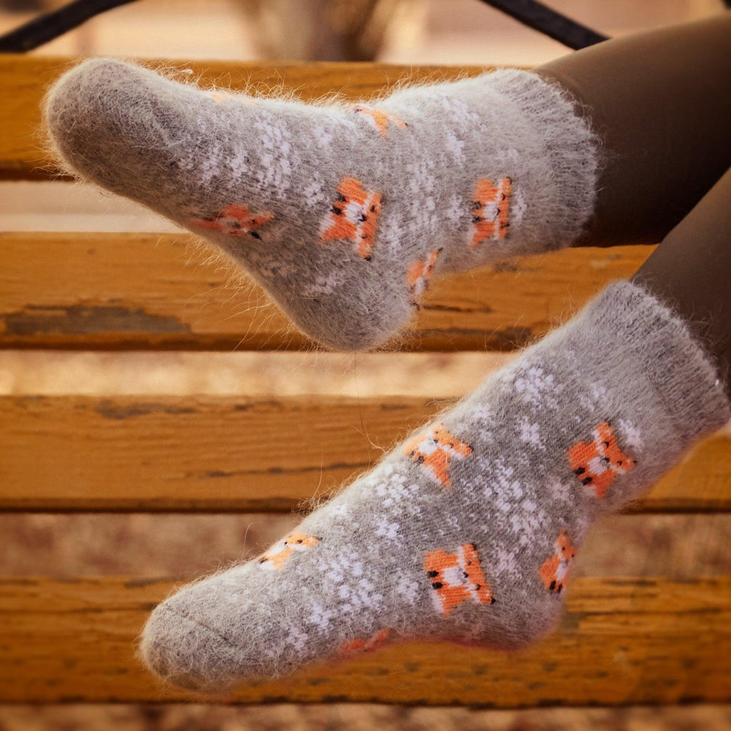 Woman's legs in outdoor settings wearing brown pants and thick goat hair grey socks with foxes and snowflakes design.
