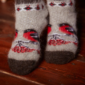 Woman's feet wearing grey and black thick goat hair socks with red birds and berries design.