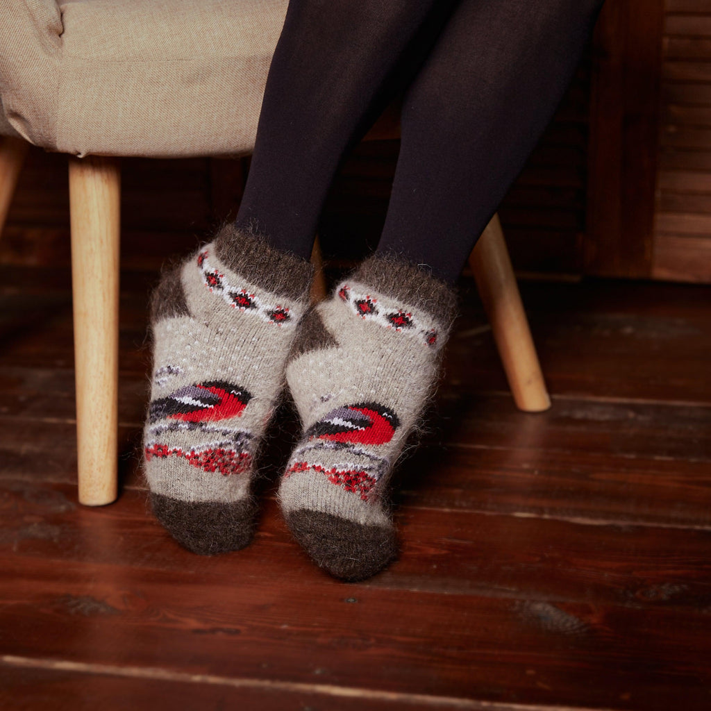 Woman's feet in home interior wearing black leggings and grey, black low-cut goat wool warm socks with red bird and berries design.